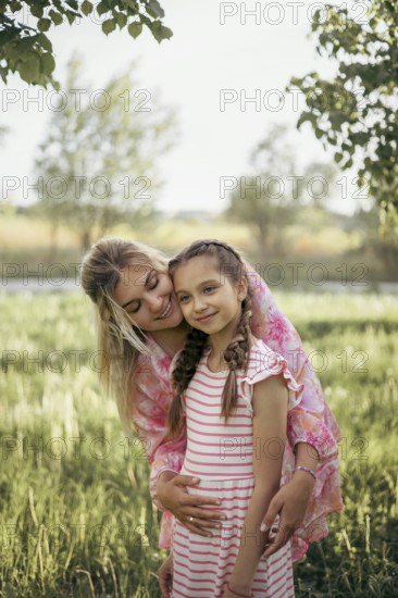 A mother gently embraces her daughter in a lush green field, radiating love and warmth Their smiles