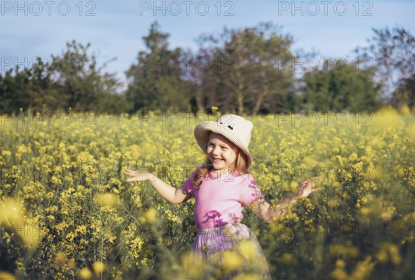 A little girl in a pink dress twirls happily among yellow flowers, embracing the beauty of nature