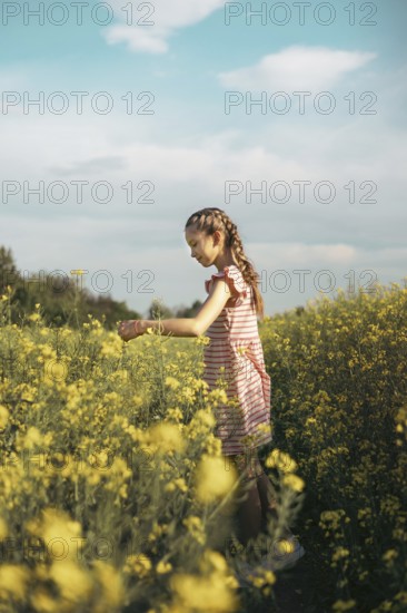 A young girl in a striped dress enjoys a peaceful moment in a blooming yellow flower field. She