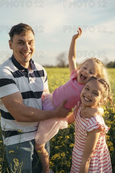 A young father and two daughters have fun together outdoors in the summer. Happy parenting and