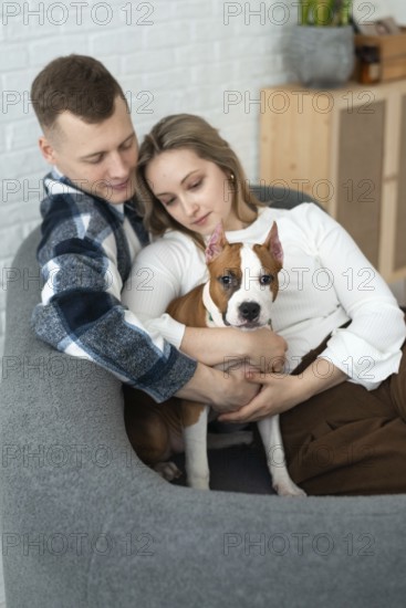 A young man and woman sit closely on a couch, affectionately holding a white and brown
