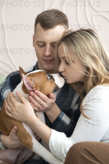 A man and woman affectionately interact with their brown and white dog in a cozy home setting,
