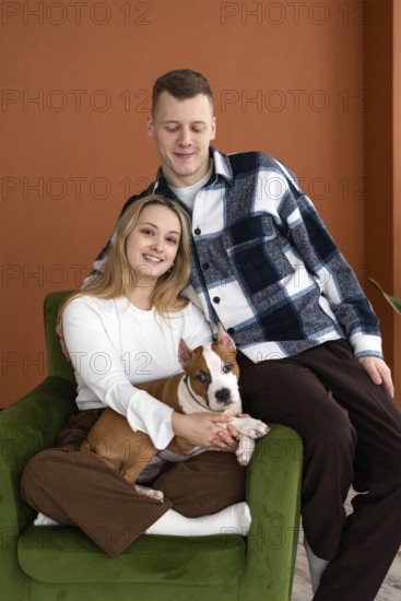 A young Caucasian man and woman smiling, seated comfortably in an armchair with their white and