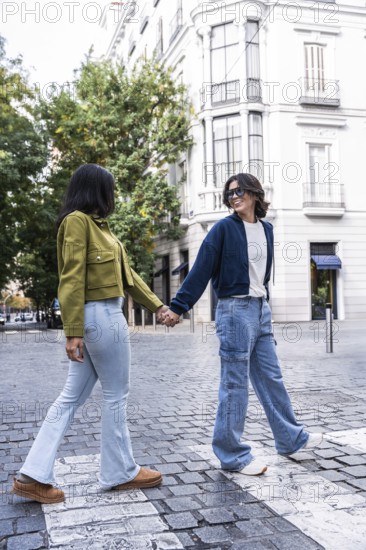 A lesbian couple holding hands while walking on a cobblestone street in the city, surrounded by