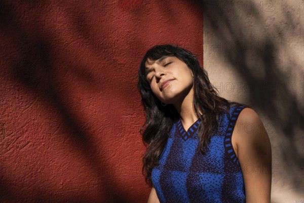 A Latin woman tilts her face toward the sunlight, eyes closed in a moment of relaxation. The warm