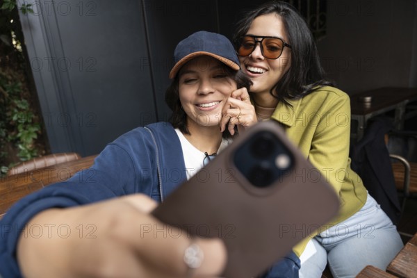 A lesbian couple is joyfully taking a selfie together outdoors, capturing their happiness and