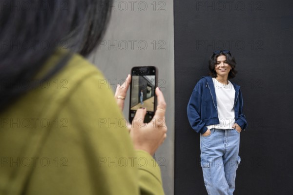 A lesbian couple enjoys a casual outdoor photoshoot. One woman wears denim and smiles against a