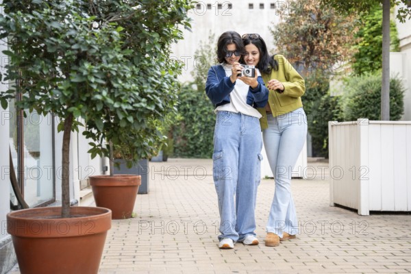 A joyful lesbian couple takes photos in a garden setting. They smile and explore the outdoors,