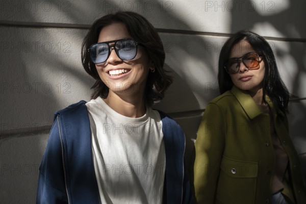 A lesbian couple enjoying the outdoors, wearing stylish sunglasses and jackets. They stand against