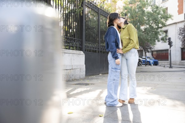 A loving lesbian couple enjoying a sunny day on a city street. They are embracing and sharing a