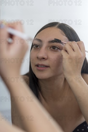 A woman concentrates while applying makeup using a brush in front of a mirror. The close up
