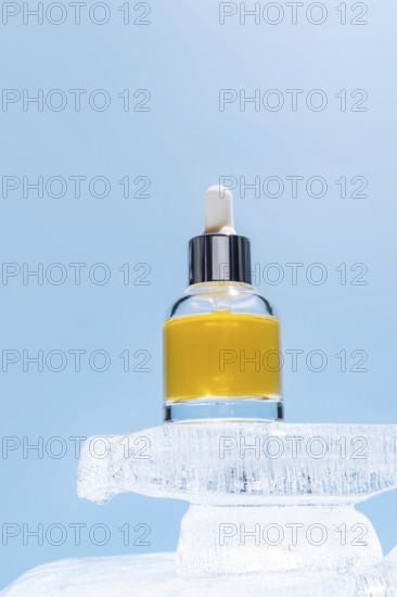 A cosmetic serum bottle with a dropper perched atop a block of ice, highlighted against a soft blue