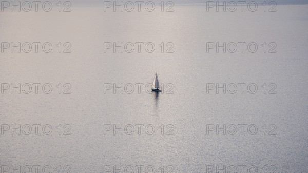 A solitary sailboat on the tranquil waters of Lake Geneva during a sunny winter day, with the snowy