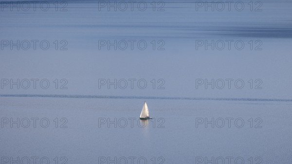A lone sailboat glides over Lake Geneva on a clear winter's day, framed by the vineyards of Lavaux