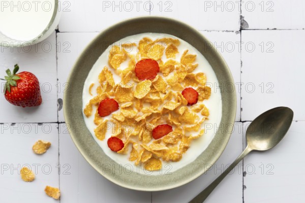 A bowl of crunchy cornflakes with fresh strawberry slices, served in milk. A wholesome breakfast
