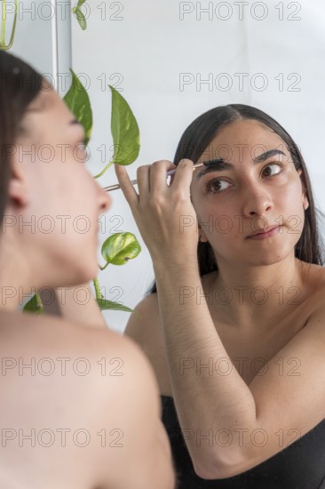 A woman focuses on applying makeup with a brush in front of a mirror for the makeup session. A