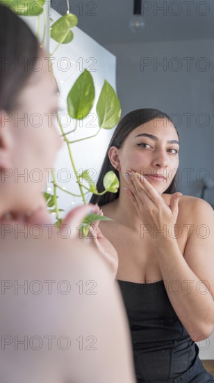 A woman is applying skincare cream while looking in the mirror. Surrounded by indoor plants, she is