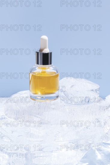 A single cosmetic serum bottle with a dropper cap, presented on a stack of clear ice cubes, under a