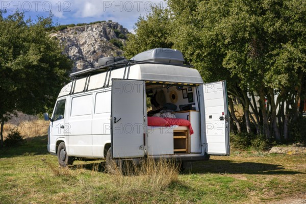 A cozy camper van with open doors reveals a comfortable interior, set against a backdrop of lush