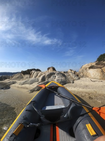 Inflatable kayak resting on a sandy shore in Greece. The vibrant kayak contrasts beautifully with