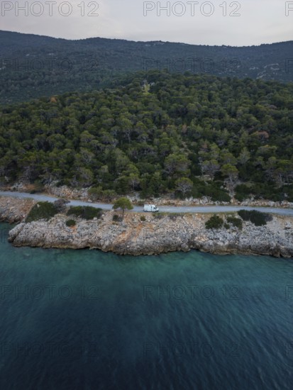 Aerial view of a van in a coastal road running through lush green forest by a turquoise sea in