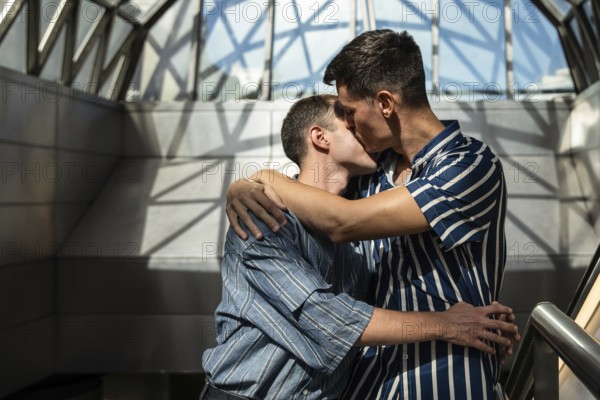 Romantic gay couple embracing and sharing a kiss in a modern architectural setting. Soft light and