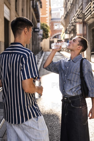 Gay couple pausing for a water break on a sunny street in Madrid. One drinks from a bottle while