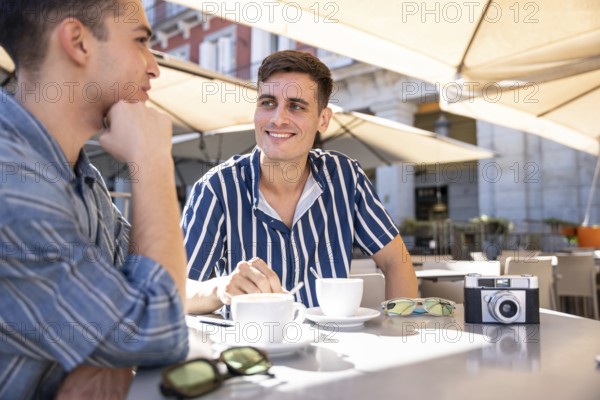 A loving gay couple enjoys a sunny coffee date on the vibrant streets of Madrid, capturing moments