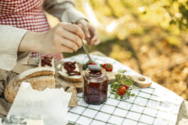 A person spreads sun-dried tomatoes on bread slices for canapes. The setup is outdoors with fresh