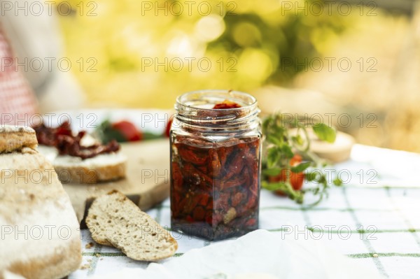 A rustic outdoor setting featuring a jar of homemade sun-dried tomatoes, fresh bread, and ripe