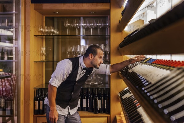 A professional sommelier meticulously selects wine bottles in a sophisticated cocktail bar,