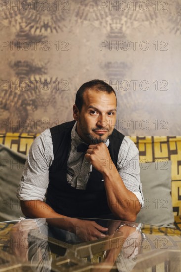 A professional bartender poses confidently in an upscale cocktail bar. Wearing a smart vest and