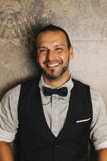 A professional bartender dressed stylishly with a bow tie, smiling warmly. The image captures the