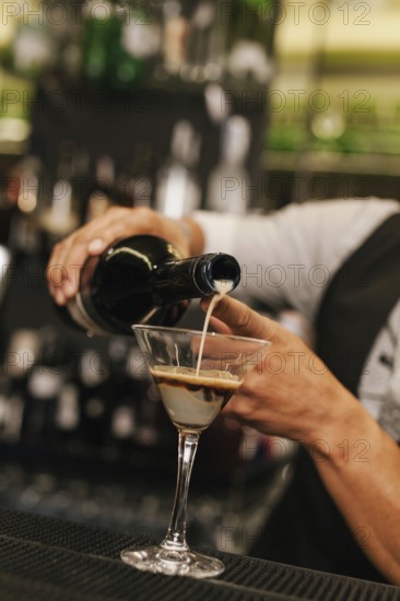 A professional bartender skillfully pours a creamy beverage into a martini glass at a modern
