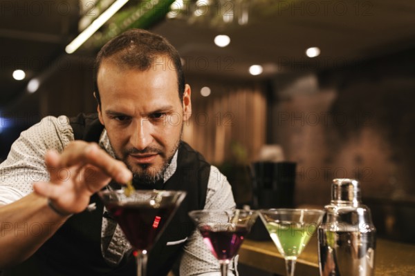 A professional bartender expertly prepares colorful cocktails in a vibrant bar. Focused and