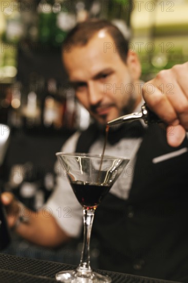 A professional bartender skillfully pours a dark liquid into a martini glass amidst an elegant