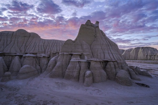 Sunset casts a soft glow over the dramatic and weathered sandstone formations of the