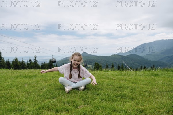 Young girl in casual attire, laughing as she sits on lush green grass at Bachledka Ski Sun in