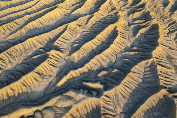 An aerial view of Caineville Mesa's golden desert textures in Utah at sunset. The rippled landscape