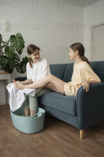 A mother and daughter enjoy a self-care routine at home, bonding over a relaxing foot bath. They