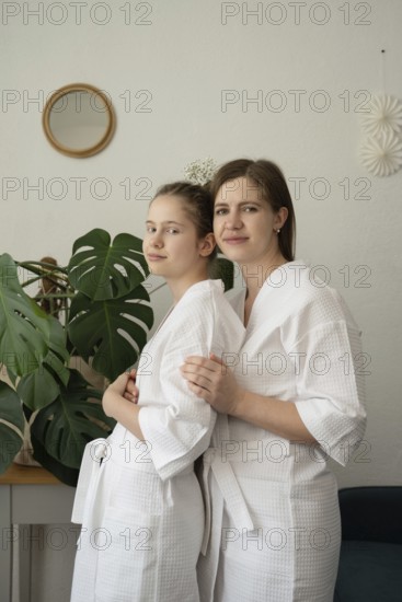 A mother and daughter are enjoying a self-care day at home. They are wearing white bathrobes,