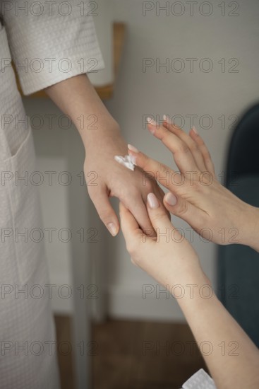 A mother and daughter enjoy a self-care day at home, gently applying lotion to each other's hands.