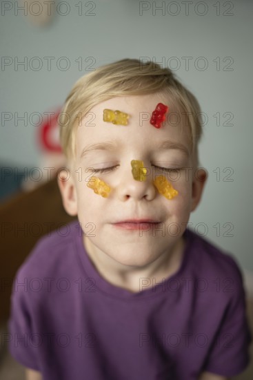 A child with closed eyes smiles blissfully with colorful gummy bears on their face, expressing a