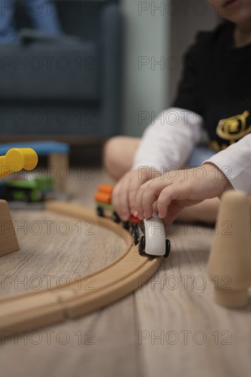 A child sits on the floor, immersed in playing with a wooden train set. The soft focus emphasizes