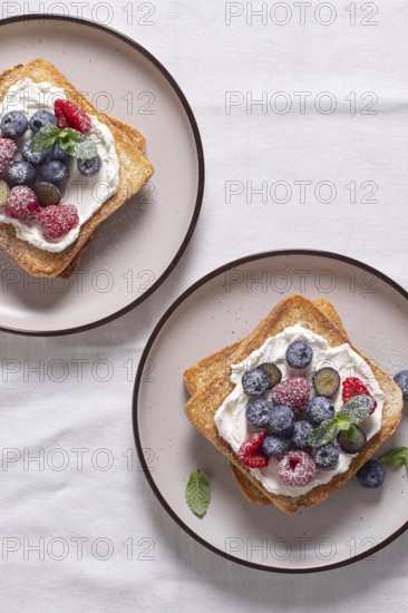 Top view of two toasts with cream cheese topped with raspberries, blueberries, and dusted with