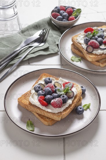 Plated serving of toast layered with cream cheese and topped with an assortment of fresh berries