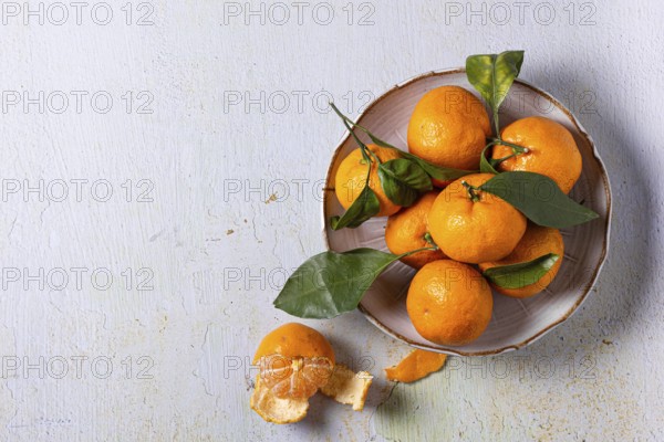 A bowl of fresh tangerines with green leaves, arranged on a textured surface. One tangerine is