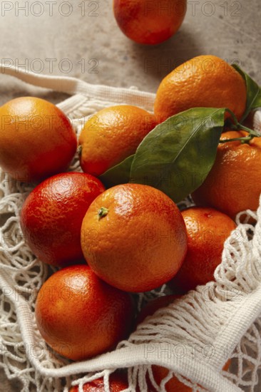 A bunch of vibrant blood oranges with deep red hues sit in a reusable cotton bag on a rustic table.