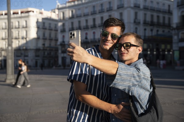A gay couple joyfully captures a selfie on the vibrant streets of Madrid. The warm sunlight