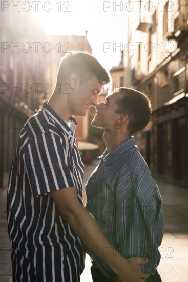 A gay couple embraces tenderly in the sunlit streets of Madrid, celebrating love and diversity. The